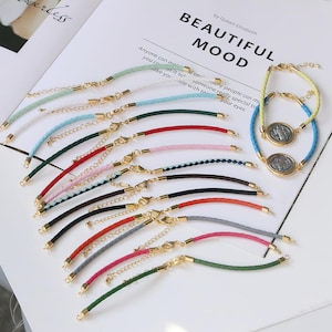 Pode incluir: Uma coleção de pulseiras coloridas com fechos dourados e cordões trançados ou lisos. Algumas pulseiras apresentam um pingente redondo em forma de moeda. As pulseiras são em várias cores, incluindo verde, branco, azul, vermelho, rosa e preto.
