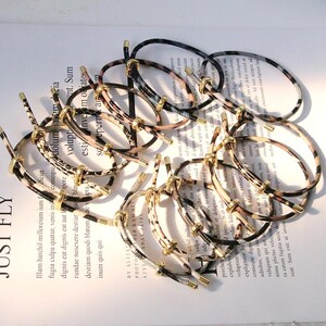 Può includere: Una collezione di elastici per capelli con dettagli in metallo color oro. Gli elastici presentano vari motivi animalier nei colori nero, marrone e crema. Gli elastici sono disposti su una superficie di carta stampata.