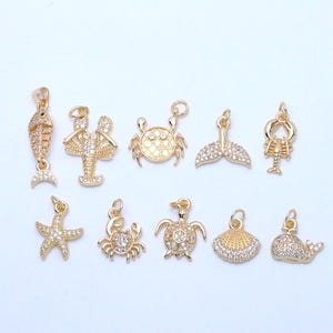 Peut inclure: Une collection de breloques dorées représentant la vie marine, dont un poisson, une langouste, un crabe, une queue de baleine, une étoile de mer, une tortue, un coquillage et une baleine. Chaque breloque est ornée de détails clairs et étincelants.