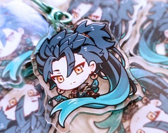 May include: A blue and green anime character keychain with a white background. The character has dark blue hair, yellow eyes, and is wearing a blue and green outfit.