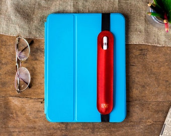 May include: A bright blue tablet case with a vertical red leather stylus holder attached by a black elastic band. The red holder features the gold embossed initials EW and contains a white stylus. The case has a smooth, tri-fold front cover.