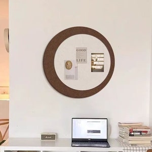 Puede incluir: Una estantería blanca con un tablero de corcho con un marco marrón y las palabras "Good Life" en él. La estantería está en una sala de estar con un sofá blanco y un portátil en el estante.