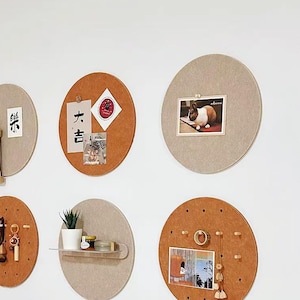 Op de afbeelding: Zes ronde kurk borden met verschillende ontwerpen en kleuren. Sommige borden hebben pinnen en andere hebben een plank. De borden hangen aan een witte muur.