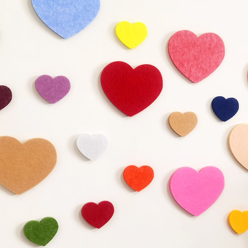 May include: A collection of felt hearts in various colors, including red, pink, blue, green, yellow, orange, and brown. The hearts are arranged on a white background.