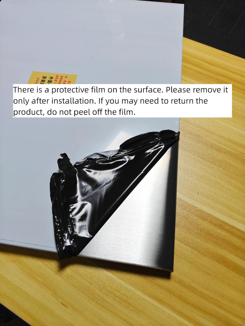 Puede incluir: Un panel met&aacute;lico rectangular con acabado plateado cepillado, parcialmente cubierto por una pel&iacute;cula protectora negra que se est&aacute; despegando. Una pegatina amarilla con texto en chino es visible en la superficie blanca del panel.