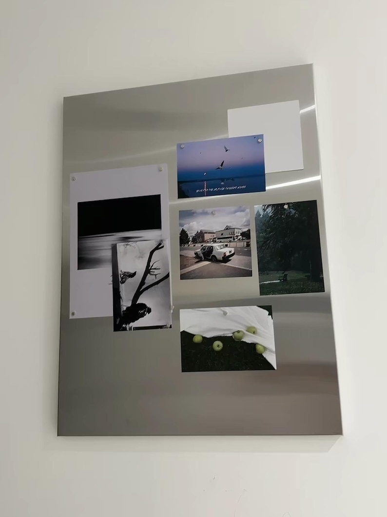 Puede incluir: Un tablero magn&eacute;tico rectangular de metal plateado que muestra varias fotograf&iacute;as y una tarjeta blanca en blanco. Las im&aacute;genes incluyen un atardecer con p&aacute;jaros, un coche en una carretera, un bosque oscuro, una silueta de &aacute;rbol en blanco y negro y manzanas verdes.