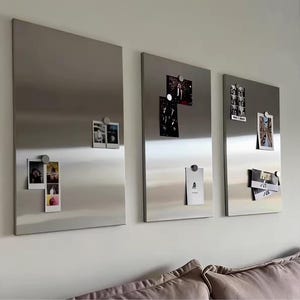 Puede incluir: Tres paneles magn&eacute;ticos rectangulares de metal plateado cepillado montados en una pared. Cada panel presenta una superficie lisa y reflectante, adornada con varias fotograf&iacute;as peque&ntilde;as e impresiones de papel sujetas por imanes circulares.