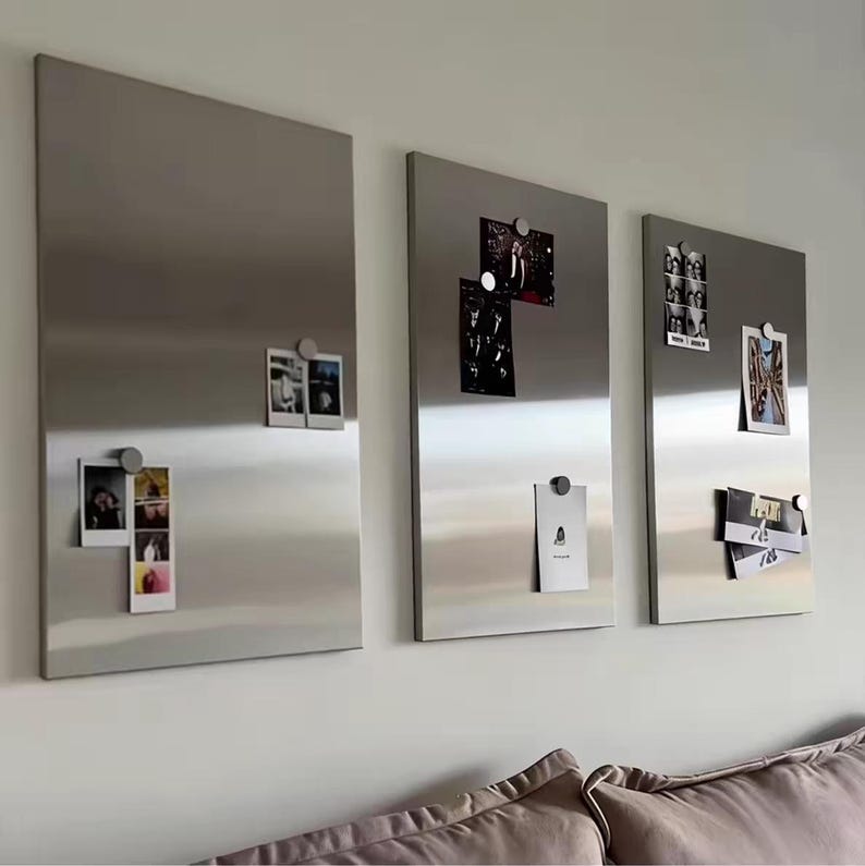Puede incluir: Tres paneles magn&eacute;ticos rectangulares de metal plateado cepillado montados en una pared. Cada panel presenta una superficie lisa y reflectante, adornada con varias fotograf&iacute;as peque&ntilde;as e impresiones de papel sujetas por imanes circulares.