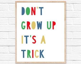 May include: A rectangular wall print in a light wood frame featuring the text DON'T GROW UP IT'S A TRICK. The letters are rendered in a sans-serif font using a vibrant color palette of blue, green, red, and yellow against a white background.