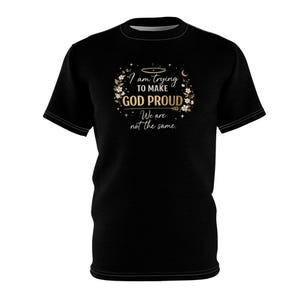 May include: Black t-shirt with the text "I am trying to make GOD PROUD. We are not the same." The text is in gold and white, surrounded by a floral design. The shirt has a crew neck and short sleeves.