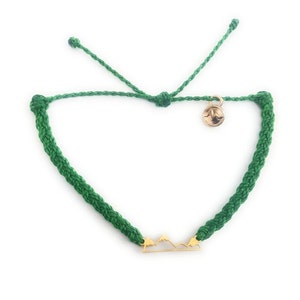Puede incluir: Pulsera de cordón trenzado verde con un dije de montaña dorado.