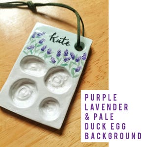 May include: A rectangular, pale green ceramic palette with four circular wells and a lavender floral design. The word "Kate" is written in cursive. A green cord is attached for hanging.