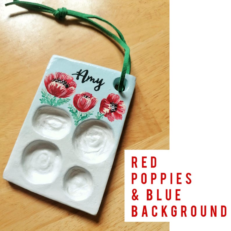 May include: A rectangular, light blue ceramic palette with five wells and a green suede cord. The palette is decorated with red poppy flowers and the name "Amy" in black script. The text "RED POPPIES & BLUE BACKGROUND" is in the lower right corner.