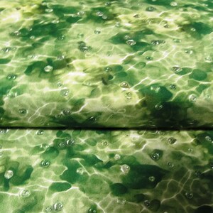 Könnte beinhalten: Nahaufnahme eines Stoffes mit wasserähnlichem Muster. Das Design zeigt Grün- und Weißtöne mit kleinen, klaren, blasenartigen Details, die über die Oberfläche verstreut sind. Der Stoff ist gefaltet und zeigt die Kontinuität des Musters.