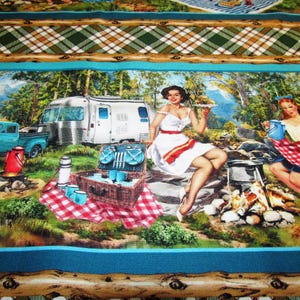 Könnte beinhalten: Ein Stoffdruck mit einer Retro-Camping-Szene, die einen silbernen Wohnwagen, einen türkisfarbenen Pickup und zwei Figuren in einem Wald zeigt. Das Design umfasst einen Picknickkorb, ein Lagerfeuer und eine rot-weiß karierte Decke.