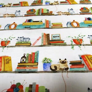 Könnte beinhalten: Weißer Stoff mit einem sich wiederholenden Muster aus Bücherregalen, Büchern, Katzen und Pflanzen. Die Regale sind mit bunten Büchern, Topfpflanzen und schlafenden Katzen gefüllt. Der Text auf den Büchern lautet "How to Live with Cats" und "Cat Training".