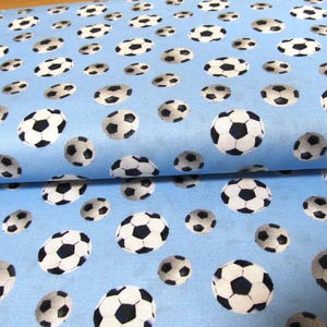 Può includere: Tessuto azzurro chiaro con un motivo ripetuto di palloni da calcio bianchi e neri. I palloni da calcio sono di varie dimensioni e sono sparsi sul tessuto. Il tessuto è piegato nell'immagine.