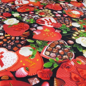 Può includere: Un tessuto nero con un motivo ripetuto di scatole a forma di cuore rosso piene di cioccolatini, rose rosse e rose bianche. Le scatole hanno nastri rossi e pois bianchi.