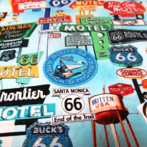 Op de afbeelding: Een kleurrijke stof met een patroon van vintage Route 66-borden. De borden zijn in verschillende kleuren en stijlen en bevatten tekst zoals "Motel", "Route 66", "America's Highway" en "Santa Monica".