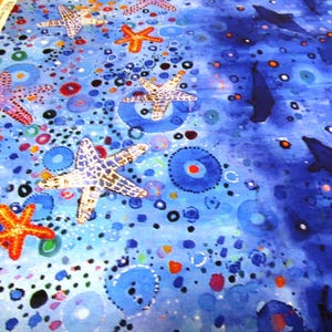 Könnte beinhalten: Stoff mit einem lebendigen Wassermotiv. Er zeigt Seesterne in Rot-, Orange- und Weißtönen sowie blaue Kreise und Punkte. Delfine schwimmen im tiefblauen Wasser und schaffen eine lebendige Unterwasserszene.