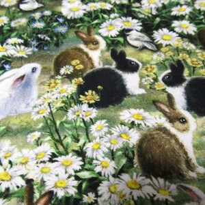 Op de afbeelding: Een close-up van een stof met een patroon van witte madeliefjes en bruine, zwarte en witte konijnen. De stof is perfect voor knutselprojecten zoals quilts, kussens en draagtassen.