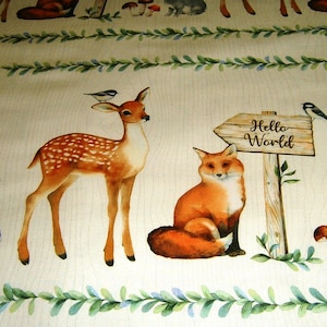 Op de afbeelding: Een beige stof met een bosmotief met een bruin hert, een rode vos, een grijs konijn en een houten bord met de tekst "Hello World".