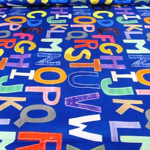 Könnte beinhalten: Ein leuchtend blauer Stoff mit einem sich wiederholenden Muster aus bunten Großbuchstaben. Die Buchstaben sind weiß umrandet und mit verschiedenen Farben gefüllt, darunter Gelb, Orange, Lila und Grün. Geeignet für Nähprojekte.