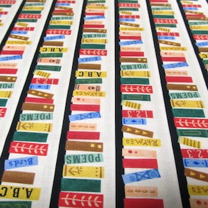 Op de afbeelding: Stof met een herhalend patroon van kleurrijke boekruggen. De ruggen zijn in verschillende kleuren, waaronder rood, geel, groen en blauw, met teksten als "Poems", "Rhymes" en "A.B.C."