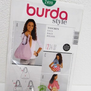 Op de afbeelding: Burda Style naaipatroonpakket met nummer 7410 op de voorkant. Het patroon is voor het maken van tassen en bevat instructies in meerdere talen. De verpakking toont drie verschillende tasmodellen, een met een roze-wit patroon, een met een rood-wit patroon en een met een geel-bruin patroon.