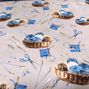 Puede incluir: Tela con un patrón repetido de cestas de hilo, agujas de tejer, tijeras y cuadrados de punto en tonos marrón, azul y blanco sobre un fondo gris. El diseño evoca un tema acogedor y hecho a mano.