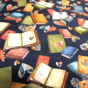 Könnte beinhalten: Ein schwarzer Stoff mit einem sich wiederholenden Muster aus offenen und geschlossenen Büchern in verschiedenen Farben wie Grün, Blau, Orange und Braun. Das Design ist mit bunten Herzformen und kleinen orangefarbenen Blumenakzenten durchsetzt.