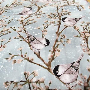 Puede incluir: Tela con un patrón repetido de pájaros posados en ramas florecidas. Los pájaros son grises y blancos con cabezas negras, sobre un fondo azul claro con motas blancas. Las ramas y las flores son en tonos marrones y crema.