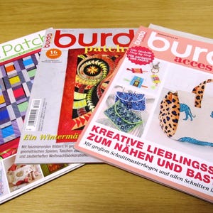 Può includere: Tre riviste con il titolo "Burda" sulla copertina. Le riviste trattano di cucito e artigianato. La rivista in alto è intitolata "Burda Patchwork" e presenta un design di trapunta patchwork colorato. La rivista al centro è intitolata "Burda Patchwork" e presenta un design di trapunta patchwork colorato. La rivista in basso è intitolata "Burda Accessoire" e presenta una borsa a mano colorata con un design a stampa leopardata.