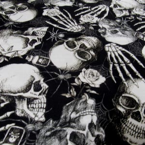 Peut inclure: Tissu noir et blanc avec un motif répété de crânes, de toiles d'araignées, d'araignées, de mains de squelettes et de roses. Les crânes ont des bouches et des orbites ouvertes. Le motif a un thème gothique ou d'Halloween.