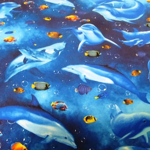 Könnte beinhalten: Ein Stoffmuster mit einer Unterwasserszene. Blaue Delfine schwimmen zwischen bunten Fischen, darunter orange, gelbe und schwarze Varianten. Blasen schweben vor dem tiefblauen Hintergrund und erzeugen ein lebendiges Wassermotiv.