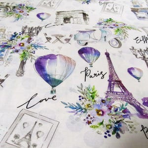 Op de afbeelding: Witte stof met een aquarelontwerp met Parijse bezienswaardigheden zoals de Eiffeltoren, de Arc de Triomphe en luchtballonnen. De woorden "Paris" en "Love" zijn in script geschreven.