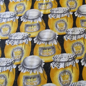 Peut inclure: Un fond noir avec un motif répété de pots de miel jaunes avec des couvercles blancs et des liens noirs. Chaque pot a une couronne et le mot "Honey" imprimé sur l'étiquette.