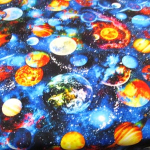 Op de afbeelding: Stof met een levendig ruimte-thema ontwerp. Het patroon toont planeten, sterren en melkwegstelsels in tinten blauw, oranje, geel en wit. Geschikt voor quilten, kleding of woondecoratie projecten.