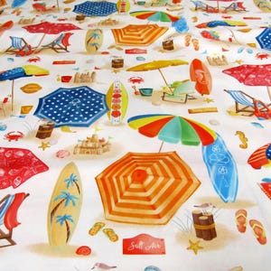 Può includere: Un tessuto bianco a tema spiaggia con ombrelloni da spiaggia colorati, tavole da surf, sedie da spiaggia, conchiglie e castelli di sabbia. Il tessuto ha la scritta "Salt Air" stampata.