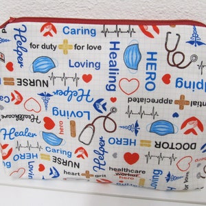 Könnte beinhalten: Eine weiße Reißverschlusstasche mit einem roten Reißverschluss. Die Tasche ist mit einem sich wiederholenden Muster aus blauen und roten medizinischen Symbolen, Herzen und Wörtern wie "Held", "Krankenschwester", "Helfer", "Sorgfältig", "Liebend" und "Heilung" bedeckt.