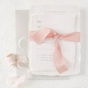 May include: A white wedding invitation with a pink ribbon tied around it. The invitation has the text "RS VP" and "sixteenth of Ma" printed on it. The invitation also has the text "number attending", "joyfully accepts", and "regretfully declines" printed on it.