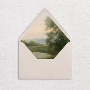 May include: A white envelope with a landscape scene printed on the front. The scene features a pond, trees, and a distant mountain range. The sky is a soft blue with a hint of pink.