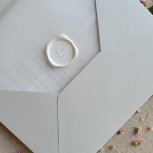 May include: A white envelope with a white wax seal with the initials "LJ" on it. The envelope is on a beige fabric background with small pink flowers.