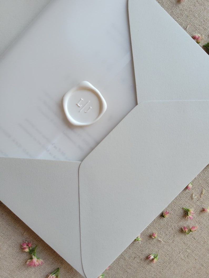 May include: A white envelope with a white wax seal with the initials "LJ" on it. The envelope is on a beige fabric background with small pink flowers.