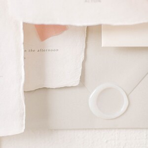 May include: A white envelope with a white wax seal. The envelope is on a white textured surface. The text "in the afternoon" is visible on a piece of paper.