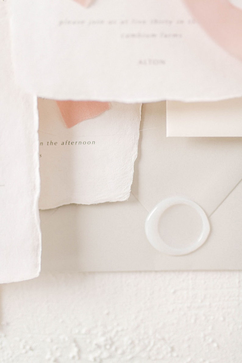 May include: A white envelope with a white wax seal. The envelope is on a white textured surface. The text "in the afternoon" is visible on a piece of paper.