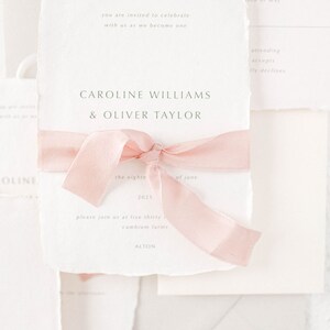 May include: A wedding invitation with a pink ribbon tied around it. The invitation is for Caroline Williams and Oliver Taylor, and it says "the eighteenth of June, 2021" and "please join us at five thirty, cambium farms, Alton".