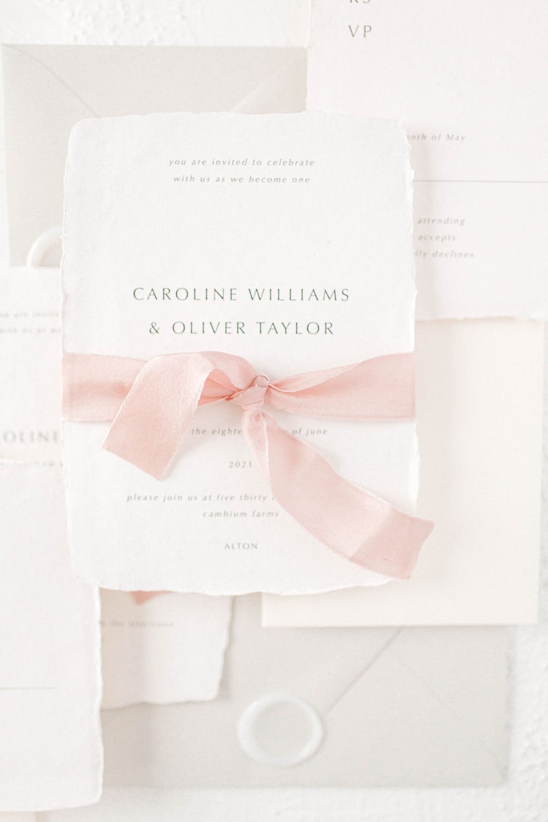 May include: A wedding invitation with a pink ribbon tied around it. The invitation is for Caroline Williams and Oliver Taylor, and it says "the eighteenth of June, 2021" and "please join us at five thirty, cambium farms, Alton".