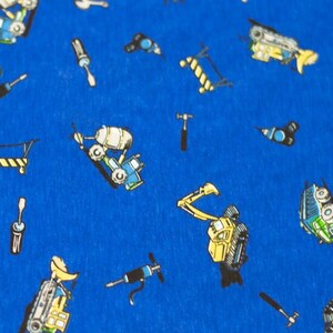 May include: A blue fabric with a repeating pattern of construction vehicles and tools. The vehicles are yellow, blue, and green. The tools are yellow, black, and red.