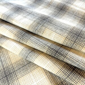May include: Close-up of a beige and gray plaid fabric with a textured weave. The fabric is folded in a few places, showing the pattern and texture.